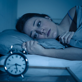 Sleepless and desperate beautiful caucasian woman awake at night not able to sleep, feeling frustrated and worried looking at clock suffering from insomnia in sleep disorder concept.